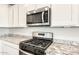 Stainless steel microwave and gas range stove with white cabinets and granite countertops at 26982 W Lone Cactus Dr, Buckeye, AZ 85396