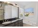 Bathroom featuring double sinks, dark cabinets, a large mirror, a tub, and natural light at 9264 E Hillery Way, Scottsdale, AZ 85260