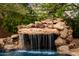 Natural rock waterfall feature enhances the pool's design and creates a tranquil outdoor space for relaxation at 4662 W Fallen Leaf Ln, Glendale, AZ 85310