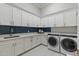 Spacious laundry room with white cabinets, blue backsplash, marble countertops, stainless steel sink, and modern washer and dryer at 2317 N Steele Cir, Mesa, AZ 85207