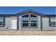 View of the home's front exterior, featuring gray siding, large windows, and a white front door at 385 W Vineyard Rd # C, Tonopah, AZ 85354