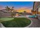 Backyard featuring a pool with rock waterfall, putting green, palm trees, and lounge chairs at dusk at 20102 E Robin Rd, Queen Creek, AZ 85142