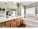 Bathroom featuring dual sinks, a large mirror, soaking tub, and wood cabinets at 23693 W La Vista Cir, Buckeye, AZ 85396