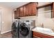 Close up of the laundry room showing stainless steel washer and dryer next to a utility sink and wood cabinetry at 12957 W Hummingbird Ter, Peoria, AZ 85383