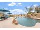 Sparkling pool features a rock waterfall, lush desert plants, and a seating area with umbrellas at 9686 W Keyser Dr, Peoria, AZ 85383