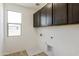 Bright laundry room features overhead storage cabinets, utility connections, and a window for natural light at 15675 W Mercer Ln, Surprise, AZ 85379