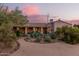 Well-landscaped backyard at dusk, featuring desert vegetation, a covered patio, and a picturesque view of the sunset sky at 38301 N 15Th Ave, Phoenix, AZ 85086