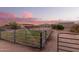 A well-maintained grass paddock is surrounded by horse facilities, including a shelter, set against a colorful sunset backdrop at 38301 N 15Th Ave, Phoenix, AZ 85086