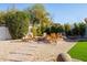 Inviting backyard sitting area featuring gravel, stone pavers, green grass, and a cozy stone fire pit with wooden Adirondack chairs at 1501 N Lesueur --, Mesa, AZ 85203