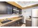 Galley kitchen featuring granite countertops, stainless steel microwave, dark cabinetry, and tile flooring at 8155 E Roosevelt St # 231, Scottsdale, AZ 85257