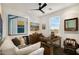 Bright living room with white sofa, ceiling fan, artwork, and wooden desk illuminated by natural window light at 15577 S 181St Ln, Goodyear, AZ 85338