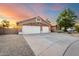 A beige two-story home featuring a stone accent, three-car garage, and desert landscaping at sunset at 20640 N 100Th Ln, Peoria, AZ 85382