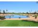 Picturesque view of a community golf course with a serene lake, green grass, and well-placed palm trees at 3685 N 162Nd Ln, Goodyear, AZ 85395