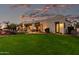 Expansive backyard with manicured lawn, patio seating, mature trees, and desert landscaping under a colorful sky at 4438 E Millbrae Ln, Gilbert, AZ 85234