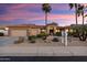 Beautiful single-story home with a three-car garage, desert landscaping, and mature palm trees at sunset at 16253 W Windcrest Dr, Surprise, AZ 85374