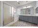 Bright bathroom featuring a large mirror, double vanity, a bathtub and glass enclosed shower at 10772 W Woodland Ave, Avondale, AZ 85323