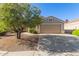 Traditional home with a two-car garage and xeriscaped front yard with a flowering tree in the desert at 12720 W Mandalay Ln, El Mirage, AZ 85335