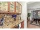 Elegant home bar boasting glass-front cabinets, wine storage, granite counters, and easy access to the dining room at 14363 W Acapulco Ln, Surprise, AZ 85379