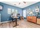 A home office with blue walls, wood floors, a work station, and a window view at 14363 W Acapulco Ln, Surprise, AZ 85379