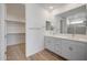 Bathroom featuring double sinks, white cabinets and countertops, with a large mirror and access to the walk in closet at 17295 W Via Dona Rd, Surprise, AZ 85387