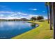 A calm lake is surrounded by green grass and a desert landscape with mountain views at 17633 W Wind Song Ave, Goodyear, AZ 85338