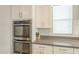 Stainless steel double ovens are surrounded by white cabinets and gray countertops at 18385 W Devonshire Ave, Goodyear, AZ 85395