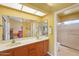 Bright bathroom featuring double sinks, wood vanity, and a shower with a glass door at 19835 N Alta Loma Dr, Sun City West, AZ 85375