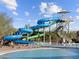 This outdoor community pool has a large blue and green water slide with a spiral design under a bright sky with puffy white clouds at 8530 W Trenton Ct, Florence, AZ 85132