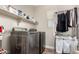 A modern laundry room featuring stainless steel washer and dryer, a storage shelf, and space to hang clothing at 15239 W Alexandria Way, Surprise, AZ 85379