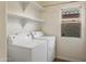 A well-lit laundry room with a window and floating shelves above the washer and dryer at 3407 W Steinbeck Dr, Anthem, AZ 85086