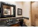 Half-bathroom with a black granite countertop, wood cabinetry, decorative mirror, and tiled walls at 6402 E Chaparral Rd, Paradise Valley, AZ 85253