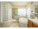 Bright and tiled bathroom area featuring glass block details, soaking tub, and vanity with sink at 18346 W Sweet Acacia Dr, Goodyear, AZ 85338
