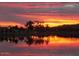 Scenic lake reflecting a vivid sunset sky with silhouetted palm trees and distant mountains at 18346 W Sweet Acacia Dr, Goodyear, AZ 85338