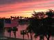 Scenic sunset view over a lake, with an American flag in the foreground and palm trees lining the shore at 18346 W Sweet Acacia Dr, Goodyear, AZ 85338