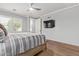Comfortable bedroom features a large window, a ceiling fan, a wall-mounted TV and wood-look tile floors at 10822 E Ramblewood Cir, Mesa, AZ 85212