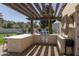 Outdoor kitchen with a stainless grill and stone surround with wood pergola and lighting at 8817 N 58Th Pl, Paradise Valley, AZ 85253