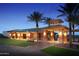 Beautifully lit clubhouse exterior at dusk, featuring palm trees, manicured lawns and brick accents at 7700 W Mockingbird Way, Florence, AZ 85132