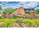 Community entrance with a large stone sign, desert landscaping, and a modern building in the background at 7722 E Fledgling Dr, Scottsdale, AZ 85255