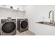 Bright laundry room features stainless steel washer and dryer, shelving, tile floors and a utility sink at 14254 W Honeysuckle Dr, Surprise, AZ 85387