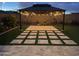 Cozy backyard featuring a stylish pergola with string lights and lush landscaping at dusk at 19864 W San Juan Ave, Litchfield Park, AZ 85340