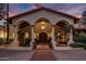 Grand home exterior with a tiled roof, arched entryway and well-manicured landscaping, lit by elegant outdoor lighting at 5254 E Arroyo Rd, Paradise Valley, AZ 85253