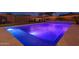 Sparkling backyard pool with vibrant blue lighting, waterfall feature, and cozy lounge seating, perfect for evening swims and relaxation at 9547 W Chama Dr, Peoria, AZ 85383