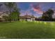 Large backyard at twilight featuring a spacious lawn, mature trees, and a charming multi-story home with balconies at 3264 E Vineyard Rd, Phoenix, AZ 85042