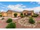 A desert landscaped yard featuring rocks and plants in front of a tan stucco home with a two-car garage at 42911 W Magic Moment Dr, Maricopa, AZ 85138