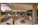 Covered patio featuring stone table, chairs, and fire pit surrounded by lush desert landscaping and hardscape at 21854 N 263Rd Dr, Buckeye, AZ 85396