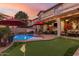Inviting backyard with a swimming pool, putting green, outdoor seating, and lush landscaping under the evening sky at 17541 W Statler Dr, Surprise, AZ 85388