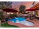 Charming backyard pool area featuring a unique design with a waterfall feature and comfortable seating under red umbrellas at 17541 W Statler Dr, Surprise, AZ 85388