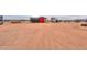 A large lot with a small red barn, trailer and covered stalls on a vast, flat expanse of desert landscape at 7209 N Maple St, Maricopa, AZ 85139