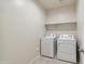 Functional laundry room features a washer, dryer, shelving, and neutral tiling at 35569 N Breezy Ln, San Tan Valley, AZ 85140