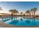 A community pool reflecting the sunset sky, surrounded by palm trees and lounge seating at 42920 W Kingfisher Dr, Maricopa, AZ 85138